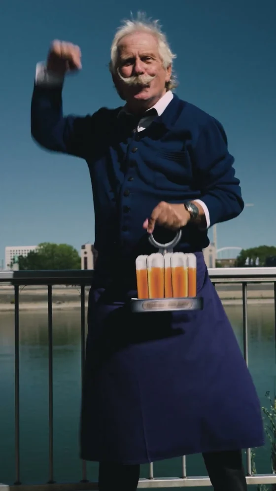 Standbild der Videobotschaft: Henning Krautmacher als K&ouml;bes mit einem Kranz K&ouml;lsch auf der Hohenzollernbr&uuml;cke.