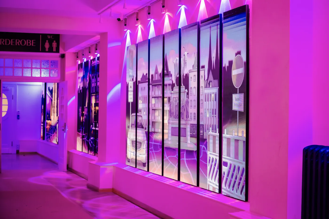 Das Foyer der Volksbühne: raumhohe LED-Stelen zeigen eine illustrierte Kölner Straßenszene, die Wände leuchten pink.